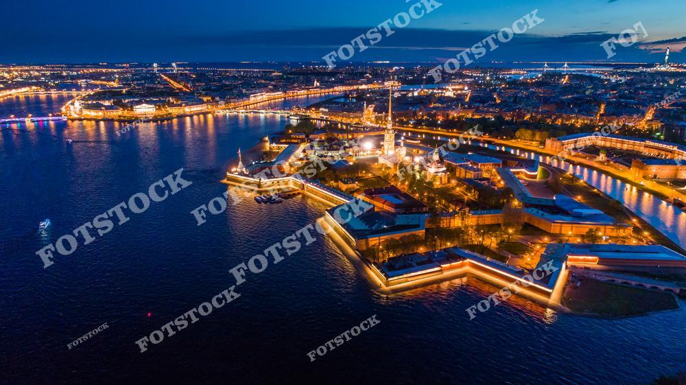 Ночной вид на Петропавловскую крепость в Санкт-Петербурге и окружающие её водные каналы с высоты птичьего полёта. Огни крепости и набережной красиво отражаются в воде Невы, создавая живописный городской пейзаж северной столицы России. Фотография подчёркивает историческое и культурное наследие города, романтику ночного Петербурга и величие архитектурного ансамбля крепости. Изображение идеально подходит для публикаций о путешествиях, аэрофотосъёмке, ночной архитектуре, туристических маршрутах и достопримечательностях Санкт-Петербурга.